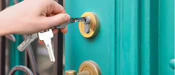 A person holding a set of house keys and inserting one inside the door lock to unlock it.